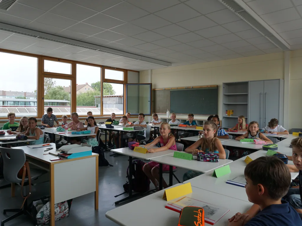 Kinder sitzen an Tischen in einem hellen Klassenraum.